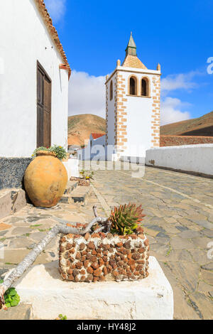 Dorfstraße mit traditionellen Häusern mit Blumentöpfen vor und Turm der Kathedrale Santa Maria de Betancuria in Betancuria Seilbahn Hintergrund Stockfoto