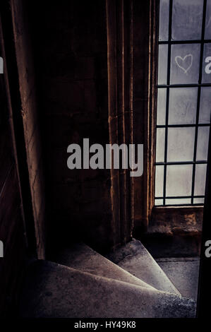 Ein Farbfoto von einem unheimlichen Treppenhaus führt nach unten mit einem staubigen alten Fenster. Ein Herz wird in den Staub auf der Fensterscheibe gezeichnet. Stockfoto