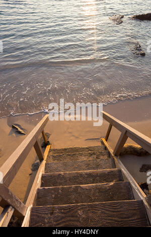 Privater Zugang zu einem öffentlichen Strand auf Oahu Hawaii bei Sonnenuntergang mit der Treppe im Mittelpunkt und das Wasser heraus verwischt. Stockfoto