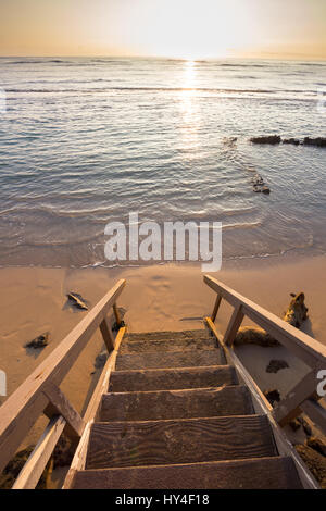 Privater Zugang zu einem öffentlichen Strand auf Oahu Hawaii bei Sonnenuntergang mit der Treppe im Mittelpunkt und das Wasser heraus verwischt. Stockfoto