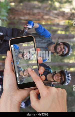Hände berühren Smartphone gegen Biker paar mit Mountainbike in Landschaft Stockfoto