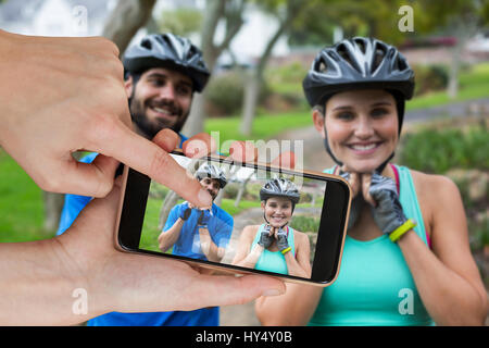 Hände berühren Smartphone gegen sportliche paar Fahrradhelm tragen Stockfoto