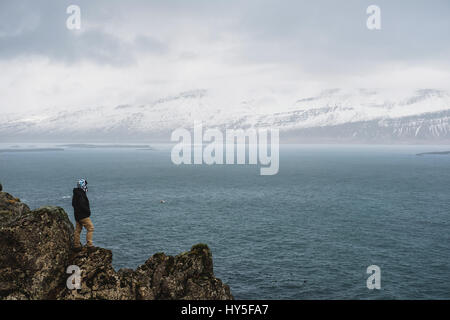 ein Mann steht auf einer Klippe mit Blick auf die Meer und Schnee Berge Stockfoto