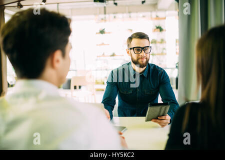 Es scheint ein guter Vorschlag. Fröhliches junges Paar Bindung zueinander und lächelnd beim betrachten einige Mann sitzt vor ihnen und gest. Stockfoto