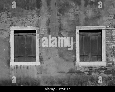 alten distressed bemalten Wand mit zwei hölzernen Fensterläden und weiße Fensterrahmen Stockfoto