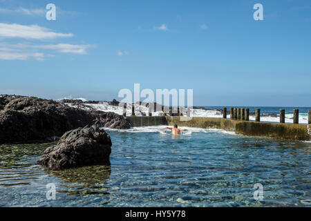 Ein Mann genießt ein erfrischendes Bad in den noch klaren blauen Gewässern des Natursteinpool an der Teneriffa-Küste in der Nähe von Alcala während Wellen von der atlantischen O Stockfoto