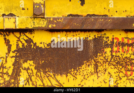 Altes rostigen Metall Container mit gelben läuten zerkratzten Lack und orange roten Buchstaben überspringen Stockfoto