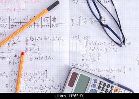 Ein Schreibtisch mit ein Schulheft, Brille, Kugelschreiber und Taschenrechner für das Studium der Mathematik Stockfoto