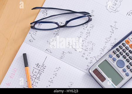 Ein Schreibtisch mit ein Schulheft, Brille, Kugelschreiber und Taschenrechner für das Studium der Mathematik Stockfoto