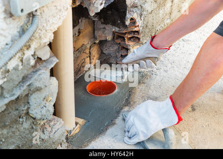 Maurer, Hause reparieren. Ein Bauarbeiter mit einer Kelle Kitt Messer während der Reparatur des Drainage-System Regenwassers auf einer Terrasse Stockfoto