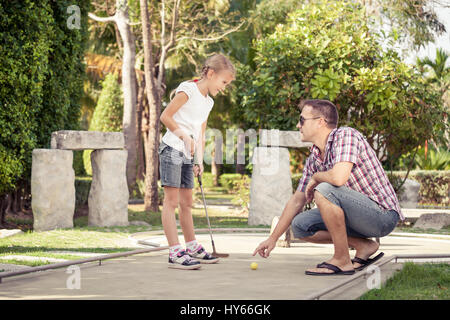 Mit Golf-Erfahrung zu teilen. Fröhlicher junger Mann seiner Tochter, Mini-Golf in der Tageszeit zu spielen.  Konzept der freundlichen Familie. Stockfoto