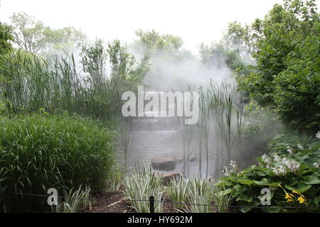 Nebel hängt über einem Wasserfall an einem kleinen Fluss zwischen den Steinen und grünen Büschen. Felsigen Bett von einem kleinen Bach im undurchdringlichen Dickicht. Rauch auf dem Wasser. Stockfoto