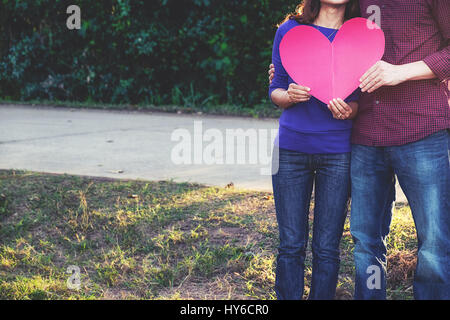 Romantisch zu zweit stehen im Park hält Papierherz. Valentinstag-Konzept Stockfoto