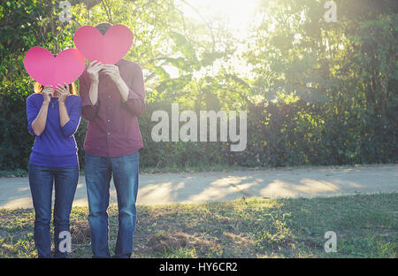 Romantisch zu zweit stehen im Park hält Papierherz. Stockfoto