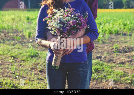 Junge liebende Paar outdoor, halten die Hände. Mann einen Blumenstrauß für seine Freundin verschenken. Natürliche Abendlicht, Fokus auf Hände und Blumen. Stockfoto