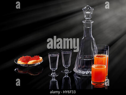 Dekanter und zwei Schnapsgläser mit Ice Wodka, zwei Lachs rot Kaviar-Sandwiches auf einer Glasplatte und zwei Gläser mit multifruit Saft auf einem schwarzen acryl Stockfoto