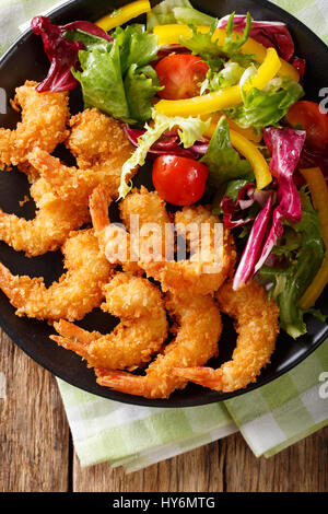 Gebratene Garnelen in Paniermehl und ein Salat aus frischem Gemüse Nahaufnahme auf einer Platte auf einem Tisch. Vertikale Ansicht von oben Stockfoto