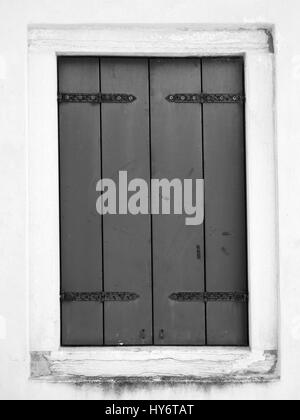 graues shuttered Fenster mit Metallscharnieren in einer weißen Wand Stockfoto