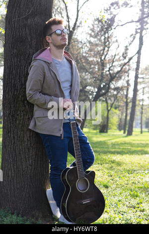 Hübscher junger Mann genießen den Park mit einer Gitarre. Tiefenschärfe und kleine Schärfentiefe. Stockfoto