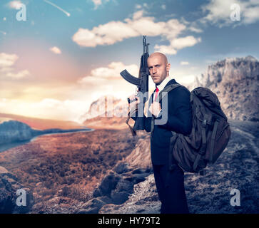 Professionelle Agenten auf geheimer Mission-Konzept. Mörder angeheuert in Anzug und roter Krawatte mit Rucksack halten Maschinengewehr in der hand Wüstental auf Zeitmessung Stockfoto