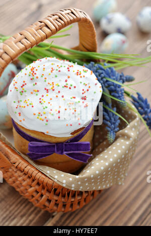 Osterkuchen im Weidenkorb mit bunten Eiern und Blumen auf hölzernen Hintergrund Stockfoto