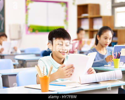 asiatische Grundschüler lesen buchen im Klassenzimmer, glücklich und lächelnd. Stockfoto