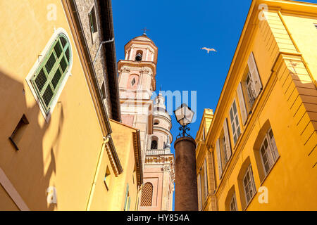 Glockenturm der Basilika Saint-Michel Archange zwischen bunten Häusern unter Blu Himmel in der Altstadt von Menton, Frankreich. Stockfoto