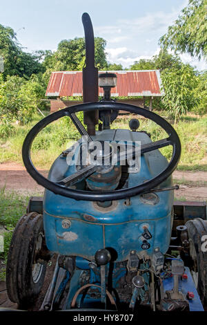 Blick ins Innere eines gebrauchten Traktors mit einem Lenkrad und die Steuerplatine. Schmutzige alte Traktor unter einem Schuppen auf dem Hof geparkt Stockfoto