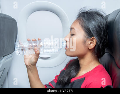 Frau im Flugzeug trinkt Wasser aus einer Plastikflasche. Ein Passagierflugzeug fliegen in das Getränk erfrischt aus seiner Flasche. Stockfoto