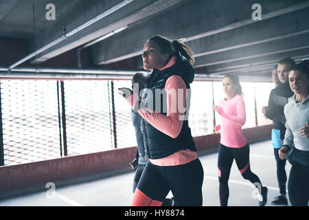 Attraktive sportliche Frau urban läuft mit einer Gruppe von verschiedenen jungen Freunde sprinten durch eine kommerzielle Tiefgarage in einer Nahaufnahme Stockfoto