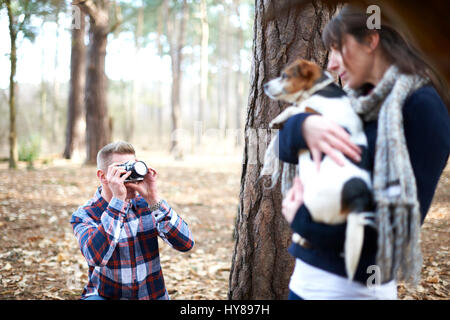 Ein Mann nimmt ein Foto von seiner Gefährtin und ihr Hund, wie sie in den Wald gehen Stockfoto