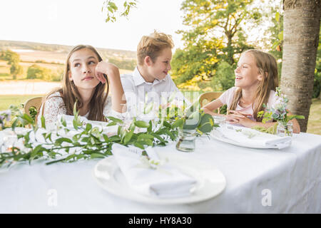 Kleine Kinder sitzen an einem Tisch draußen in der Sonne Stockfoto