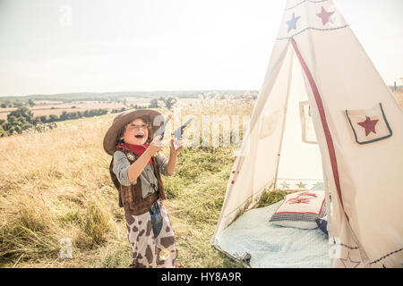 Ein kleiner Junge spielt Cowboys und Indianer draußen in der Sonne Stockfoto