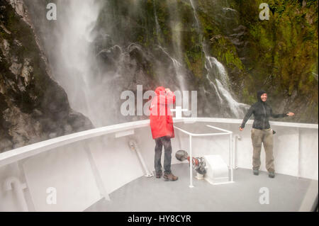 Touristen, die in der Nähe eines Wasserfalls im Milford Sound, Mammutt Nationalpark, Neuseeland Kreuzfahrt Stockfoto