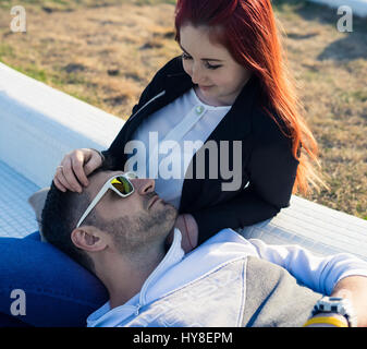 Liebe Augenblick. Bärtige erwachsener Mann mit Sonnenbrille auf dem Bein des roten Mädchenakt liegend. Stockfoto
