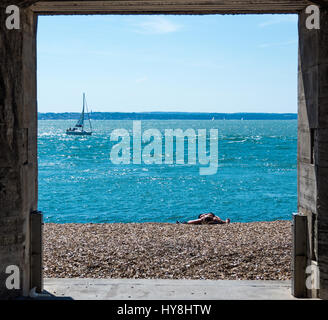 Ein Blick durch die Sally Port in Old Portsmouth mit einer Frau, Sonnenbaden am Strand, während eine Yacht durch segelt Stockfoto