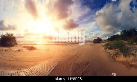 Sonnenuntergang am Südstrand. Südküste bei Sonnenuntergang. Abendhelle Sonne auf goldenem Sand. Holzweg am Strand. Schöne Anlage-Hintergrund. Stockfoto