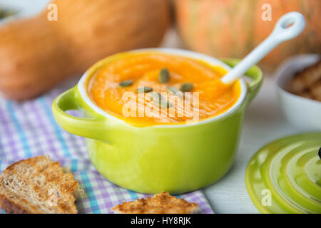 Nahaufnahme von cremige Kürbissuppe, garniert mit Kürbiskernen und Brot in grüne Schüssel auf Serviette Stockfoto