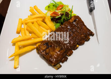 Pork Ribs Steak frites und Gemüse auf weißen Teller, in Scheiben geschnitten gebratene Grill Schweinerippchen, Schwerpunkt in Scheiben geschnittene Fleisch Stockfoto