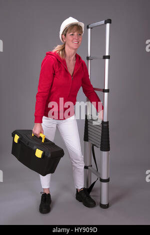 Arbeitnehmerin trägt einen Schutzhelm und hält eine Teleskop Leiter Stockfoto