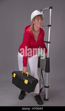 Arbeitnehmerin trägt einen Schutzhelm und hält eine Teleskop Leiter Stockfoto