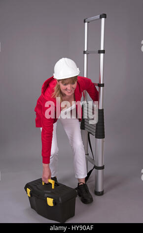 Arbeitnehmerin trägt einen Schutzhelm und hält eine Teleskop Leiter Stockfoto