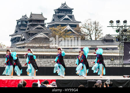 Hinokuni Yosakoi Dance Festival in Japan. Team von Reife Frauen tanzen auf der Bühne in Schwarz und Türkis Kostüm mit Kumamoto Schloss im Hintergrund. Stockfoto