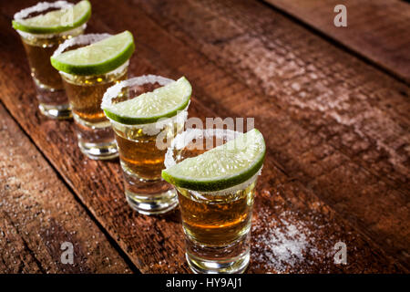 Gold Tequila Shots mit Kalk Früchten auf hölzernen Hintergrund Stockfoto