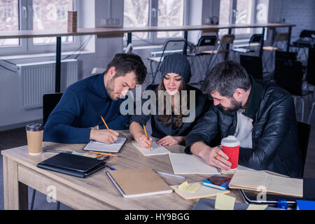 Junge Studenten in Notizblöcke oder Notebooks im Hörsaal zu schreiben. Arbeitsumfeld mit Laptop, Kaffee, Notizblöcke und Briefpapier. Stockfoto