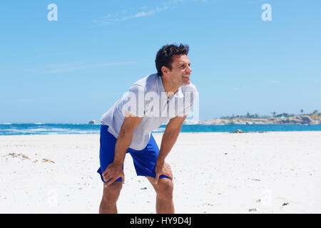 Porträt von ein gut aussehender Mann stehend mit den Händen auf die Knie am Strand Stockfoto