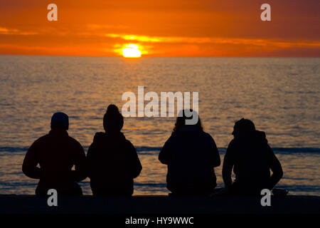 Aberystwyth, Wales, UK. 2. April 2017. UK-Wetter: Vier junge Leute sitzen in Silhouette wacht die untergehende Sonne über Cardigan Bay Aberystwyth Wales, am Ende eines Tages voller herrlich warmes Wetter und ungebrochene blauer Himmel Bildnachweis: Keith Morris/Alamy Live News Stockfoto