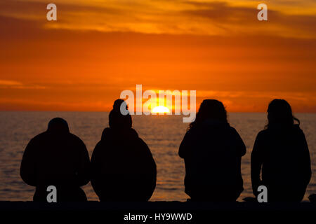 Aberystwyth, Wales, UK. 2. April 2017. UK-Wetter: Vier junge Leute sitzen in Silhouette wacht die untergehende Sonne über Cardigan Bay Aberystwyth Wales, am Ende eines Tages voller herrlich warmes Wetter und ungebrochene blauer Himmel Bildnachweis: Keith Morris/Alamy Live News Stockfoto