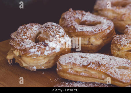 Auswahl an frisch gebackene Windbeutel und Eclairs mit Vanillecreme gefüllt und mit Puderzucker auf rustikalem Holzbrett, Nahaufnahme Stockfoto