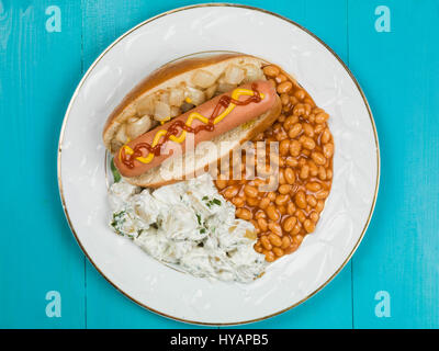 Hot Dog in einem Brötchen mit Baked Beans und Kartoffelsalat auf blauem Grund Stockfoto